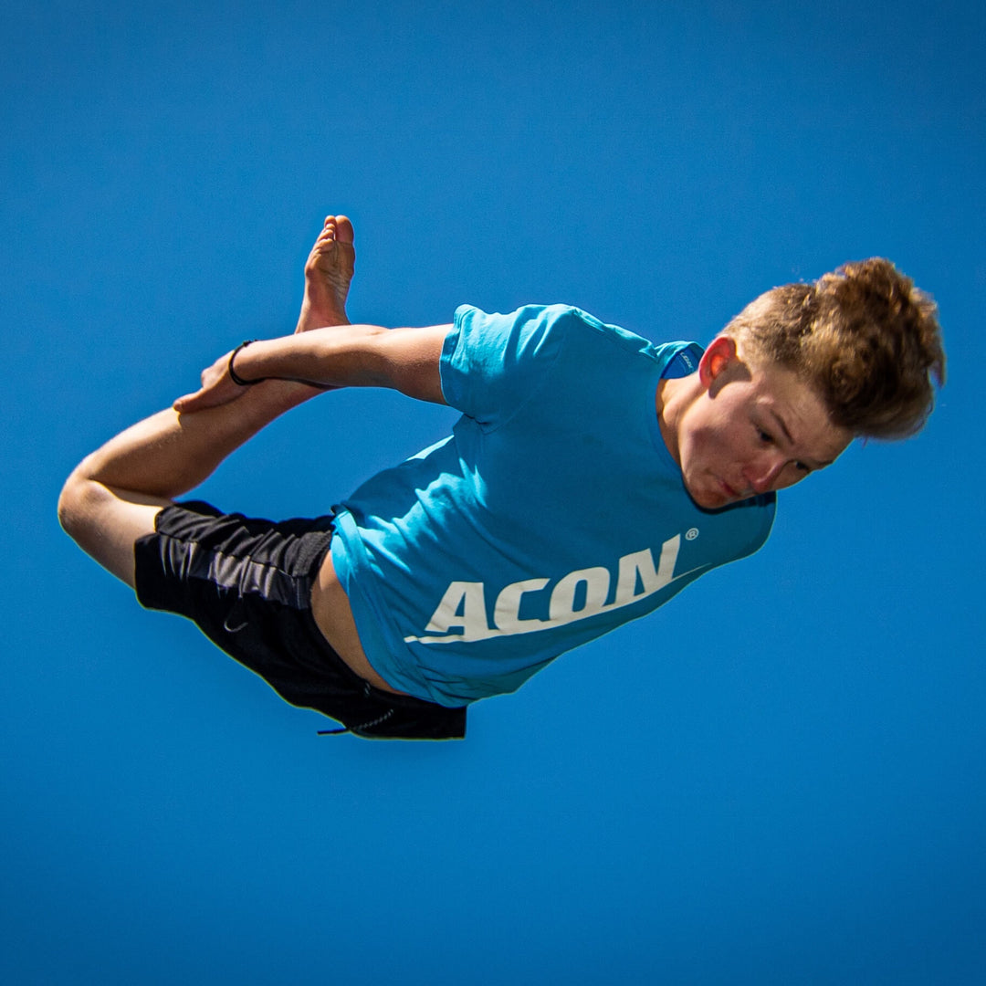 Ein Junge in einem blauen ACON-T-Shirt beim Trampolinspringen.