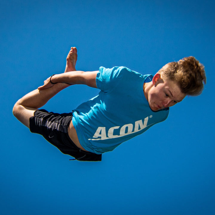 Ein Junge in einem blauen ACON-T-Shirt beim Trampolinspringen.