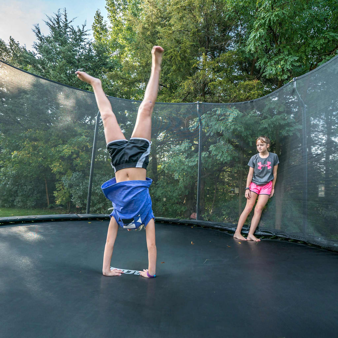 Ein Mädchen macht Handstand auf einem Acon-Trampolin, ein Freund schaut zu.