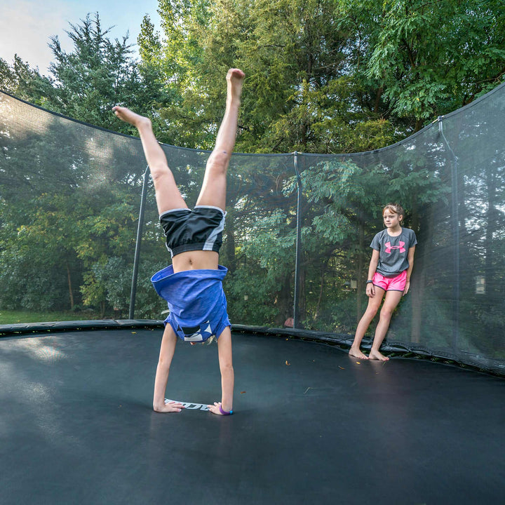 Ein Mädchen macht Handstand auf einem Acon-Trampolin, ein Freund schaut zu.