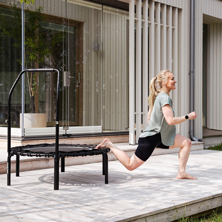 Eine Frau macht Beugeübungen auf einem Acon FIT Balance-Rebounder auf der Terrasse eines Hauses.